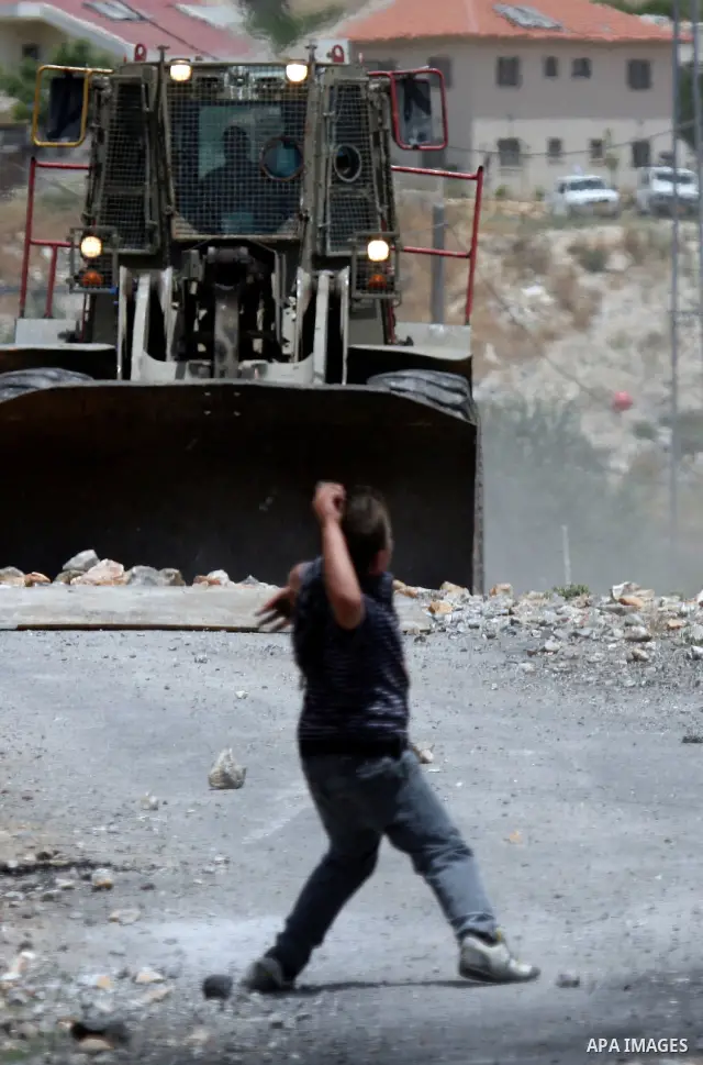 A Palestinian protester throws stone at an Israeli army bulldozer during clashes in the northern West Bank village of Kufr Qaddum, near the Jewish settlement of Kdumim, on May 25, 2012. Photo by Wagdi Eshtayah