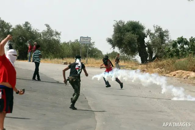 Palestinian protesters run away from tear gas during clashes between stone throwers and Israeli soldiers in the West Bank village of Nabi Saleh, near Ramallah, on May 25, 2012 following a protest against the confiscation...