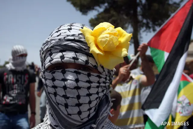 A masked Palestinian protester holds a flower on his head during clashes between stone throwers and Israeli soldiers in the West Bank village of Nabi Saleh, near Ramallah, on May 25, 2012 following a protest against the...