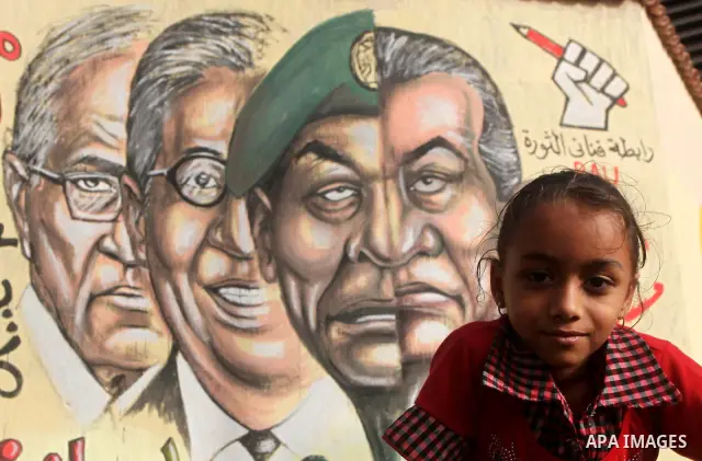 A Egyptian girl sit in front of a mural depicting presidential candidate Ahmed Shafiq (L) and a combination of the faces of former president Hosni Mubarak and Field Marshal Mohamed Hussein Tantawi at Tahrir Square in Cai...