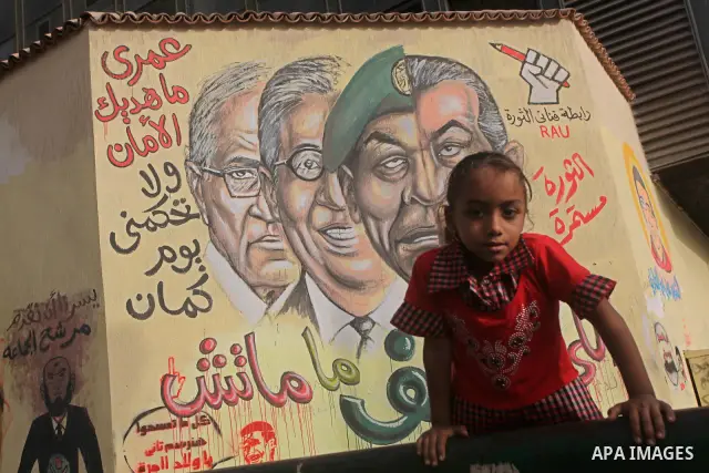 A Egyptian girl sit in front of a mural depicting presidential candidate Ahmed Shafiq (L) and a combination of the faces of former president Hosni Mubarak and Field Marshal Mohamed Hussein Tantawi at Tahrir Square in Cai...