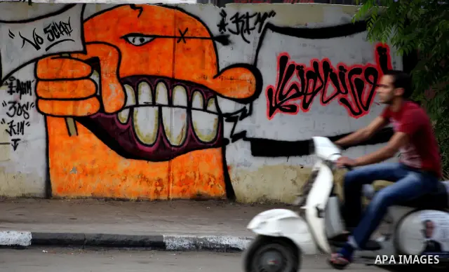 Egyptians walk past graffiti depicting a chained ballot box being controlled by the ruling military council at Tahrir Square in Cairo on May 25, 2012. Egyptians reacted nervously to the first results of their presidentia...