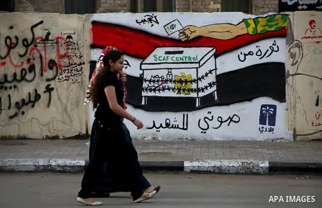 Egyptians walk past graffiti depicting a chained ballot box being controlled by the ruling military council at Tahrir Square in Cairo on May 25, 2012. Egyptians reacted nervously to the first results of their presidentia...