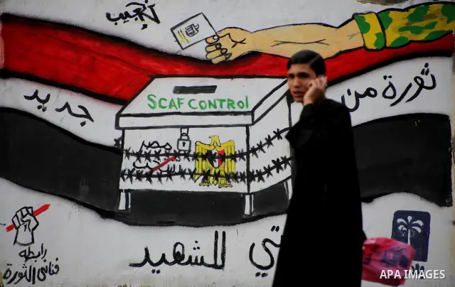 Egyptians walk past graffiti depicting a chained ballot box being controlled by the ruling military council at Tahrir Square in Cairo on May 25, 2012. Egyptians reacted nervously to the first results of their presidentia...