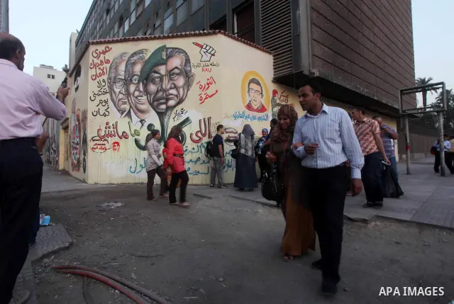 Egyptians walk in front of a wall sprayed graffiti at Tahrir Square in Cairo May 30, 2012. An arson attack on the headquarters of one of the two candidates in Egypt's presidential election has marred campaigning for the...