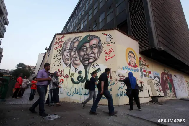 Egyptians walk in front of a wall sprayed graffiti at Tahrir Square in Cairo May 30, 2012. An arson attack on the headquarters of one of the two candidates in Egypt's presidential election has marred campaigning for the...