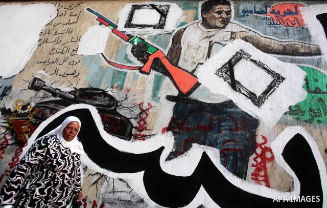Egyptians walk in front of a wall sprayed graffiti at Tahrir Square in Cairo May 30, 2012. An arson attack on the headquarters of one of the two candidates in Egypt's presidential election has marred campaigning for the...