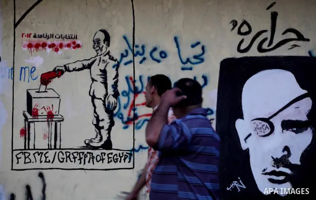 Egyptians walk in front of a wall sprayed graffiti at Tahrir Square in Cairo May 30, 2012. An arson attack on the headquarters of one of the two candidates in Egypt's presidential election has marred campaigning for the...