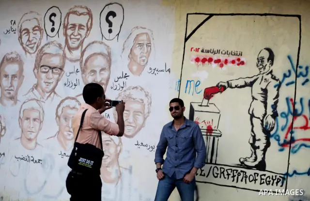 Egyptians walk in front of a wall sprayed graffiti at Tahrir Square in Cairo May 30, 2012. An arson attack on the headquarters of one of the two candidates in Egypt's presidential election has marred campaigning for the...
