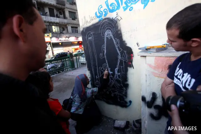 Egyptians walk in front of a wall sprayed graffiti at Tahrir Square in Cairo May 30, 2012. An arson attack on the headquarters of one of the two candidates in Egypt's presidential election has marred campaigning for the...