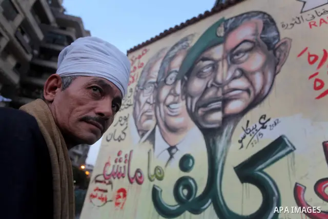 Egyptians walk in front of a wall sprayed graffiti at Tahrir Square in Cairo May 30, 2012. An arson attack on the headquarters of one of the two candidates in Egypt's presidential election has marred campaigning for the...