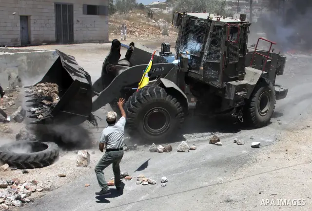 Palestinian protester throws stones toward Israeli military bulldozer during clashes after a demonstration against the nearby Jewish settlement of Kdumim, in the West Bank village of Kfar Kadum, near Nablus June 8, 2012....