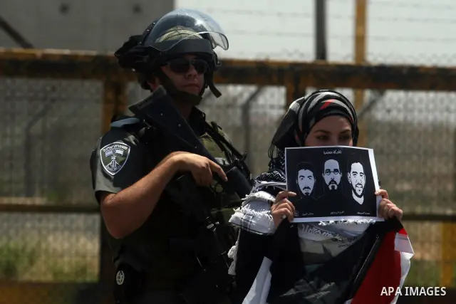 Israeli police keep guard as female Palestinian protestors fly their national flag and hold pictures of jailed Palestinian football player Mahmud Sarsak (R) and prisoners Akram Rikhawi (C) and Samir al-Baraka during a de...