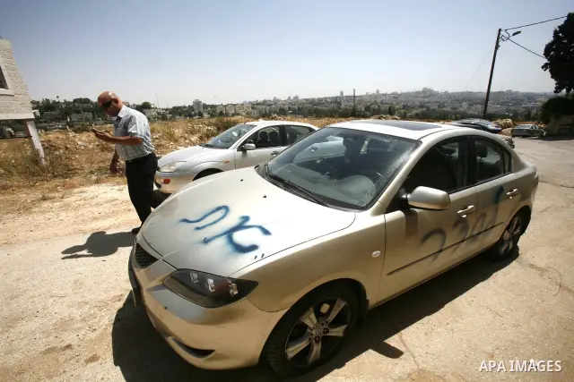 A Palestinian man gestures towards a car sprayed with graffiti written in Hebrew that reads, "Ulpena" referring to the Jewish outpost built illegally in the West Bank and which is earmarked to be relocated following a su...