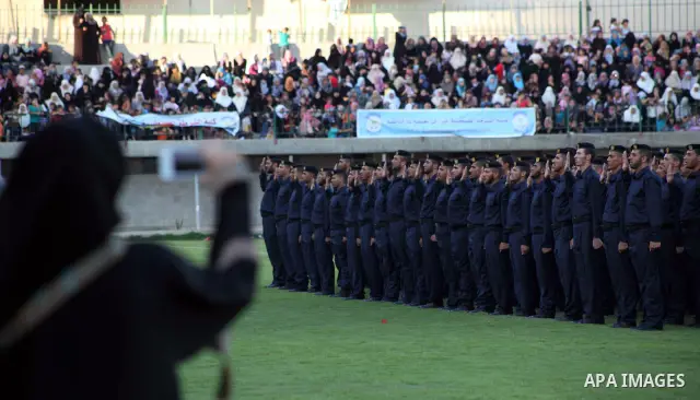 Palestinian woman looks on as graduating police officers stand to attention during a ceremony at the police academy in Gaza City on June 13, 2012, making them the first batch of officers to graduate after four years of t...