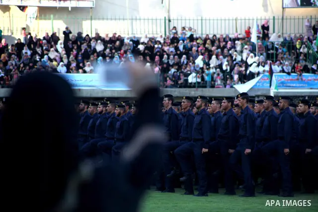 Palestinian woman looks on as graduating police officers stand to attention during a ceremony at the police academy in Gaza City on June 13, 2012, making them the first batch of officers to graduate after four years of t...
