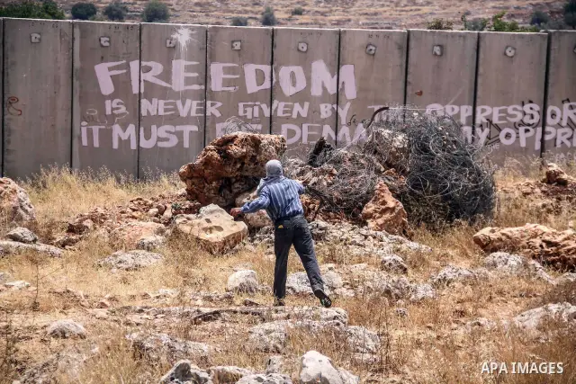 Palestinian protester hurls stones at Israeli soldiers during a weekly demonstration against Israel's controversial separation barrier in the West Bank village of Nilin on June 15, 2012. When completed, 85 percent of the...