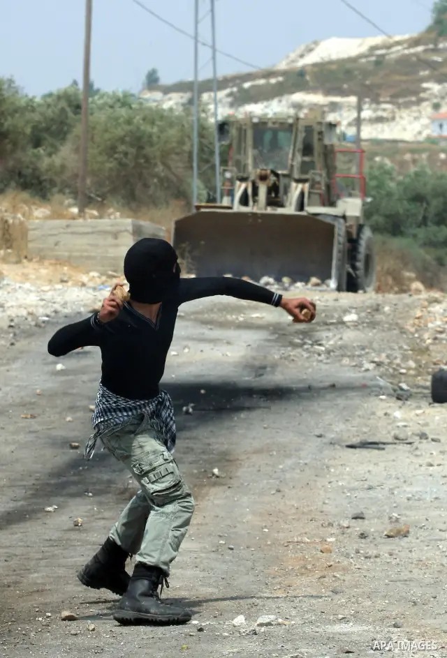 A Palestinian protester throws stone at an Israeli army bulldozer during clashes in the northern West Bank village of Kufr Qaddum, after the weekly protest against the expansion of the nearby Jewish settlement of Kdumim,...