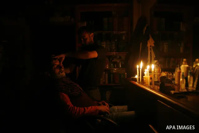 A Palestinian barber cuts hair for youths and lighting a candle during a power outage in a barber shop in Rafah, southern Gaza Strip on June 16, 2012. Photo by Eyad Al Baba
