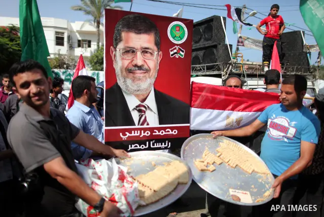 Palestinian Hamas supporter distributes sweets as others hold up Egyptian flags and the poster of the Muslim Brotherhood's presidential candidate Mohammed Morsi in the streets of Gaza City, 18 June 2012. Egypt's Muslim B...