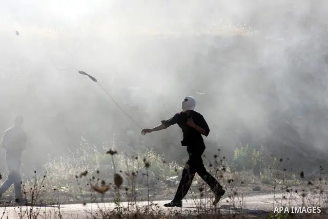 A Palestinian protestor throws stones using a sling shot during clashes with Israeli police following a demonstration outside Ofer prison, near the West Bank city of Ramallah, in solidarity with Palestinian prisoners bei...