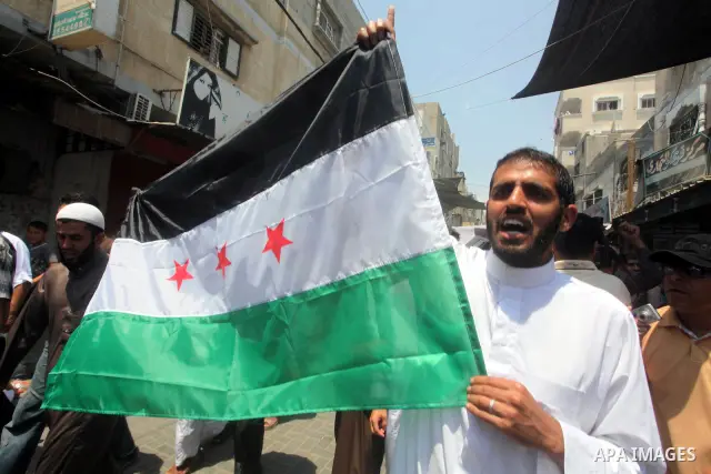 Palestinians hold a Syrian revolution flag during a protest against Syria's President Bashar al-Assad and in support of Syrian civilians at Nusseirat refugee camp in the central Gaza Strip on June 22, 2012. The French fo...