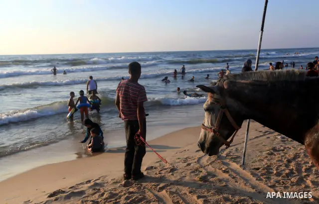 A Palestinian man sells toys on his cart as others enjoy swimming in the sea on Gaza's beach on 27 June 2012 in Gaza. Photo by Majdi Fathi