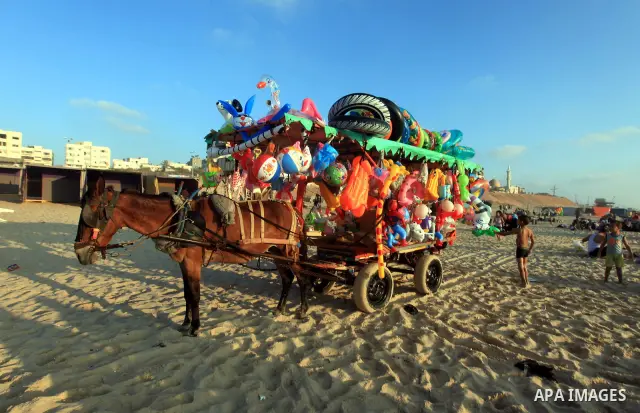 A Palestinian man sells toys on his cart as others enjoy swimming in the sea on Gaza's beach on 27 June 2012 in Gaza. Photo by Majdi Fathi