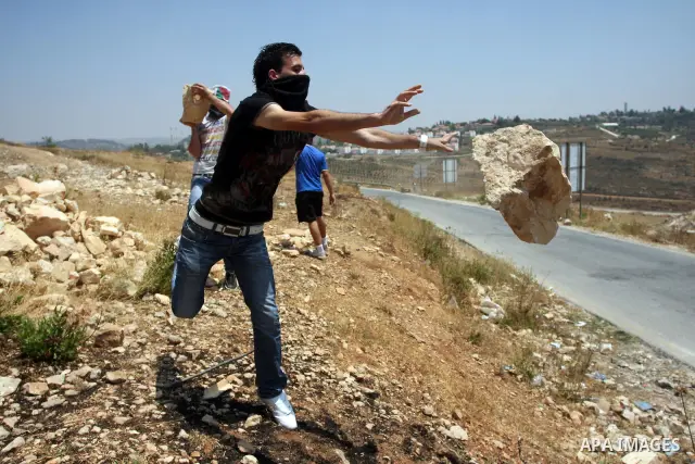 A Palestinian protester throws a big stone on the road during a demonstration against Israel's separation barrier in the West Bank village of Nabi Saleh near Ramallah, , Friday, June 29, 2012. Palestinians protest weekly...