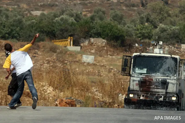 A Palestinian protester throws stones toward Israeli truck during clashes following a weekly demonstration against Israel's separation barrier and the neighbouring Jewish settlement of Halamish in the West Bank village o...