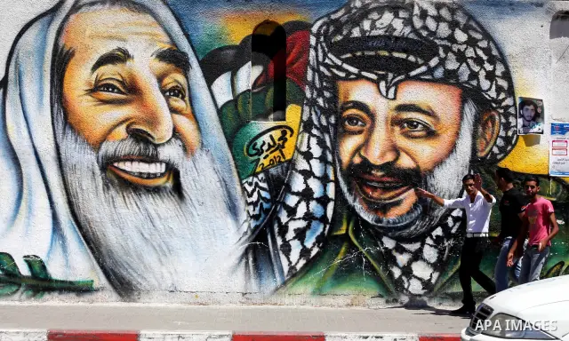 Palestinian youths walk past a mural depicting late Hamas spiritual leader Sheikh Ahmed Yassin (L) and late Palestinian leader Yasser Arafat (R) in Gaza City on July 4, 2012. Arafat, who died in 2004, was poisoned by pol...