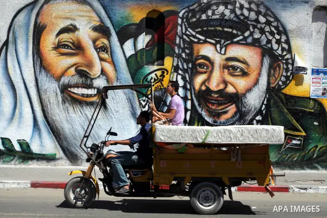 Palestinians ride a motorcycle past a mural depicting late Hamas spiritual leader Sheikh Ahmed Yassin (L) and late Palestinian leader Yasser Arafat (R) in Gaza City on July 4, 2012. Arafat, who died in 2004, was poisoned...