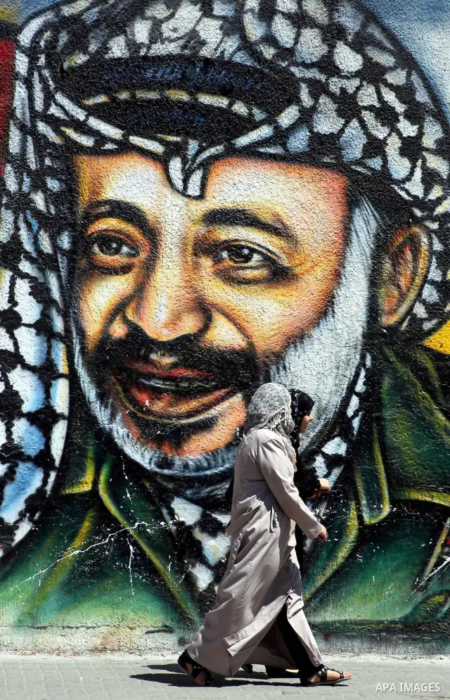 Palestinian women walk past a mural depicting late Hamas spiritual leader Sheikh Ahmed Yassin (L) and late Palestinian leader Yasser Arafat (R) in Gaza City on July 4, 2012. Arafat, who died in 2004, was poisoned by polo...