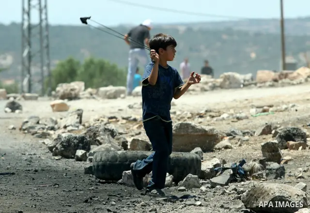 A Palestinian child throws stones towards Israeli border police during a protest against the expansion of the nearby Jewish settlement of Kdumim, in the northern West Bank village of Kufr Qaddum, on 06 July 2012. Photo b...