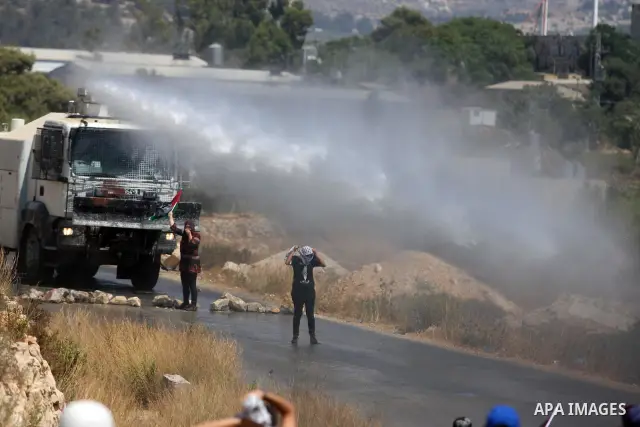 Palestinian protestors wave a Palestinian flag in front of a truck spraying foul smelling water during clashes with Israeli soldiers at a weekly protest against a nearby Jewish settlement, in the West Bank village of Nab...
