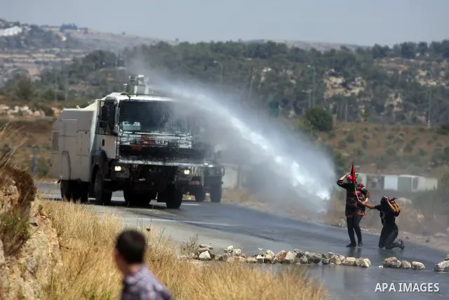 Palestinian protestors wave a Palestinian flag in front of a truck spraying foul smelling water during clashes with Israeli soldiers at a weekly protest against a nearby Jewish settlement, in the West Bank village of Nab...