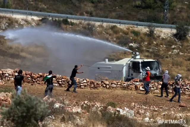 Palestinian protesters throw stones towards an Israeli truck spraying foul smelling water during clashes with Israeli soldiers at a weekly protest against a nearby Jewish settlement, in the West Bank village of Nabi Sale...