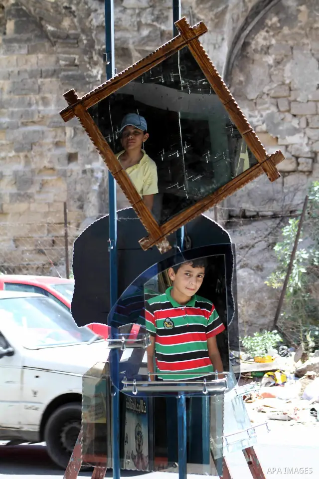 Palestinians are reflected in mirrors for sale as they walk through a traditional market in the refugee camp of Jabaliya, in the northern Gaza Strip, 07 July 2012 . Photo by Ashraf Amra