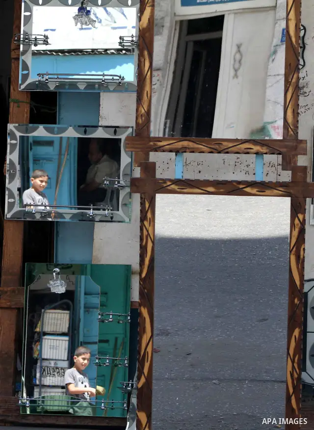 Palestinians are reflected in mirrors for sale as they walk through a traditional market in the refugee camp of Jabaliya, in the northern Gaza Strip, 07 July 2012 . Photo by Ashraf Amra