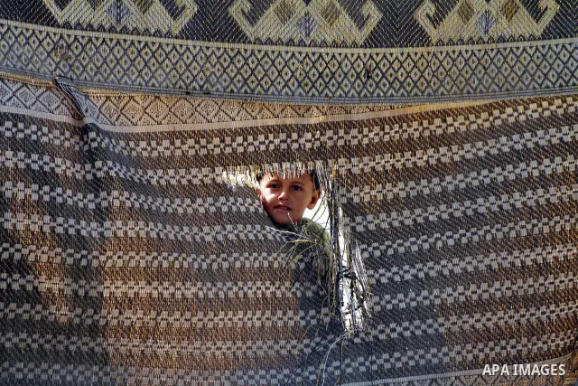 A Palestinian child looks through a mat of straw in front her home in Zeitoun neighborhood southern Gaza city on 09 July 2012. Photo by Ashraf Amra