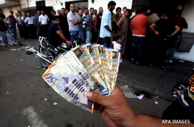 A Palestinian man displays his salary after withdrawing it from an automated teller machine of the Bank of Palestine in Gaza city on July 12, 2012. The Palestinian Authority announced that it will give only 60% of the sa...