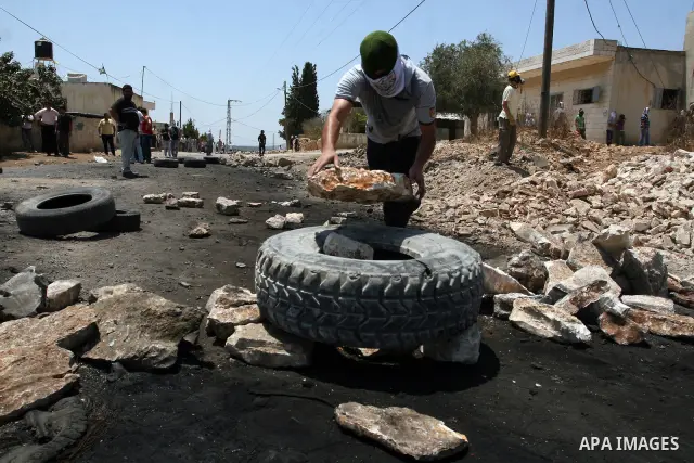 A Palestinian protester prepares a tire to burn it during clashes with Israeli security forces following a weekly protest against the nearby Jewish settlement of Kdumim, in the West Bank village of Kufr Qaddum, near Nabl...