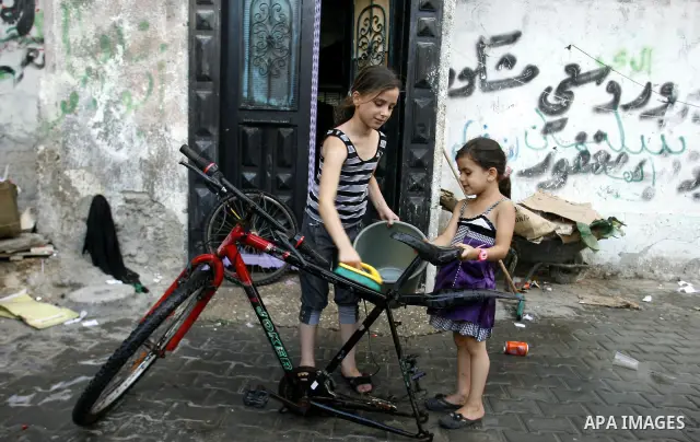 Palestinian children clean the motorcycle at water as hot weather hits the southern Gaza Strip. Photo by Eyad Al Baba