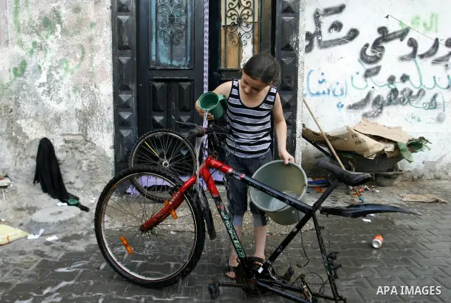 A Palestinian child cleans the motorcycle at water as hot weather hits the southern Gaza Strip. Photo by Eyad Al Baba