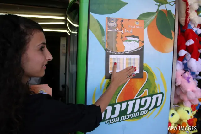 A Palestinian protestor hangs a placard during a protest demanding Palestinian merchants to boycott Israeli settlement products and goods, and support national economy in the West Bank city of Ramallah ,on July 15, 2012....