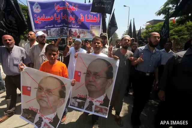 A Palestinian supporter of the Popular Resistance Movement linked Hamas, holds a sword as others carry posters of Myanmar's President Thein Sein during a demonstration calling to stop killing the Burmese Muslims in Myanm...