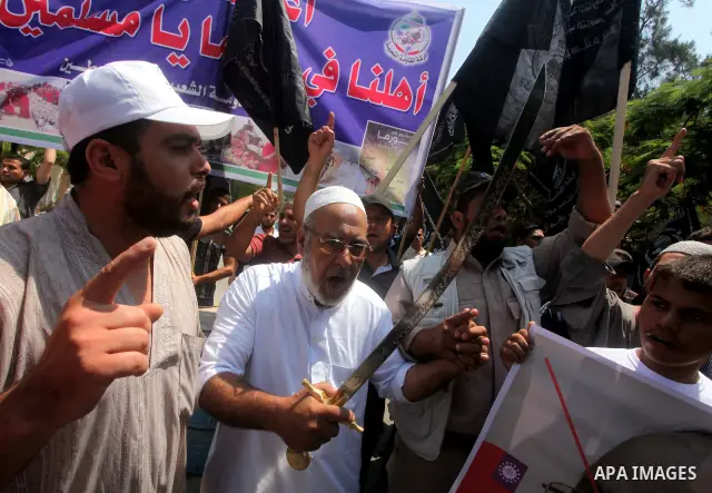 A Palestinian supporter of the Popular Resistance Movement linked Hamas, holds a sword as others carry posters of Myanmar's President Thein Sein during a demonstration calling to stop killing the Burmese Muslims in Myanm...