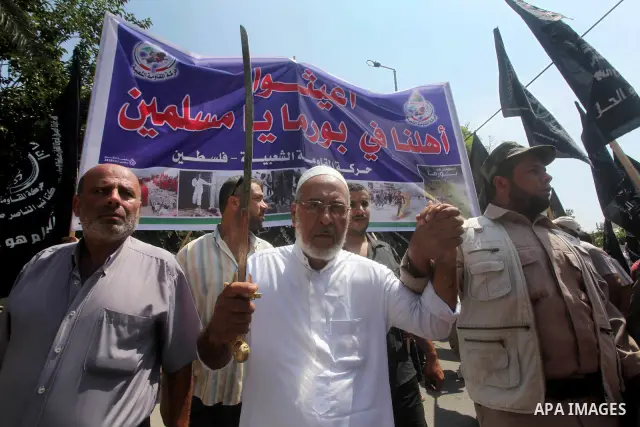 A Palestinian supporter of the Popular Resistance Movement linked Hamas, holds a sword as others carry posters of Myanmar's President Thein Sein during a demonstration calling to stop killing the Burmese Muslims in Myanm...