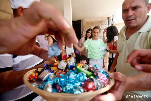A Palestinian man gives candy after heard the results of final exams of his high school daughter known as "Tawjihi" in Jerusalem, on July 19, 2012. The Ministry of Education in Gaza Strip announced the final results coin...