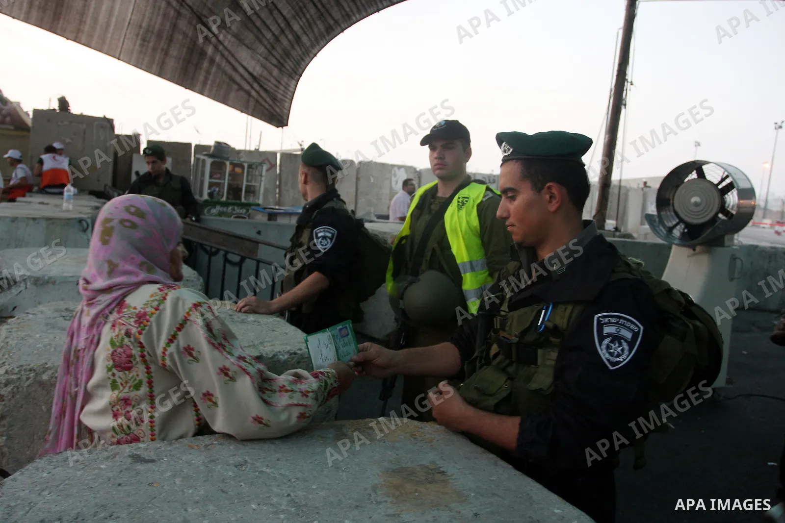 An Israeli border police officer checks documents of Palestinian women who wait to cross the Qalandia checkpoint on the outskirts of the West Bank city of Ramallah on July 20, 2012 as they head to the Al-Aqsa mosque comp...